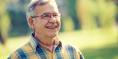 Older man with glasses in middle of field smiling