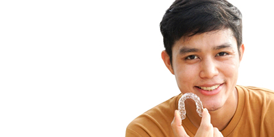 Asian man in an orange shirt holding ClearCorrect aligner